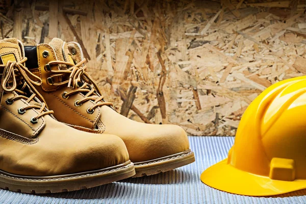 Pair of working boots and yellow construction helmet on plywood — Stock Photo, Image