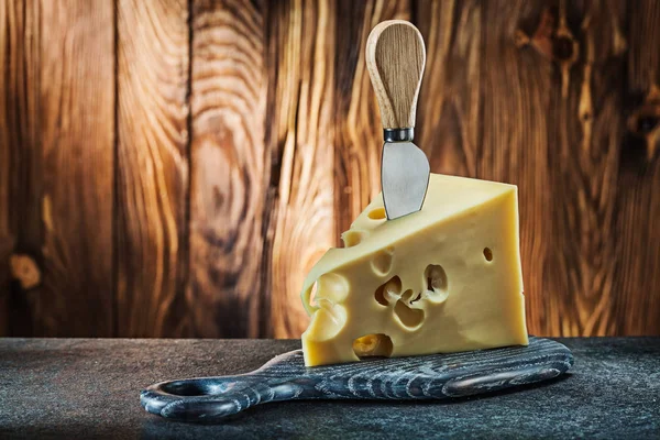 Pedazo de queso de leche maasdam con cuchillo en la tabla de cortar poco —  Fotos de Stock