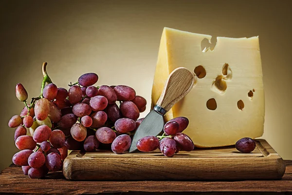 Pezzo grosso di formaggio con uva rosata e coltellino su b di legno — Foto Stock