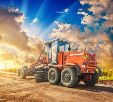 Klasik inşaat traktörü, tekerlekler üzerinde, yol kenarında duruyor. Güzel günbatımı manzarası.