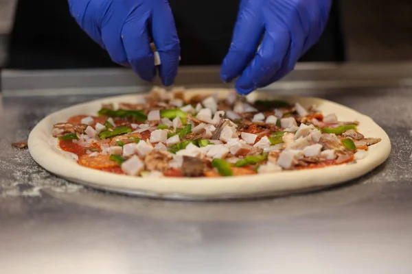 Making pizza in a restaurant, chef hands in gloves