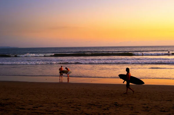 風光明媚な日没で インドネシア バリ島のビーチに歩いてサーファー — ストック写真