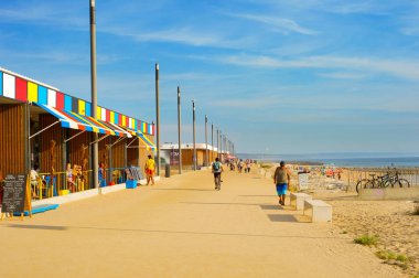 COSTA DA CAPARICA, LISBON, PORTUGAL - SEPTEMBER 17, 2018: People walking by seaside promenade in the sunny summer day. Costa de Caparica is the famous tourist destination clipart