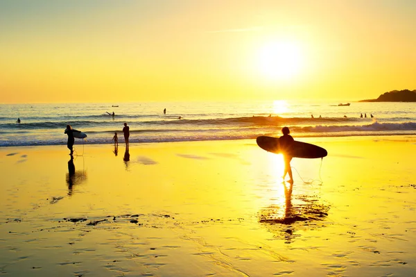 日落时在葡萄牙阿尔加维沙滩上散步到海边的冲浪者剪影 — 图库照片