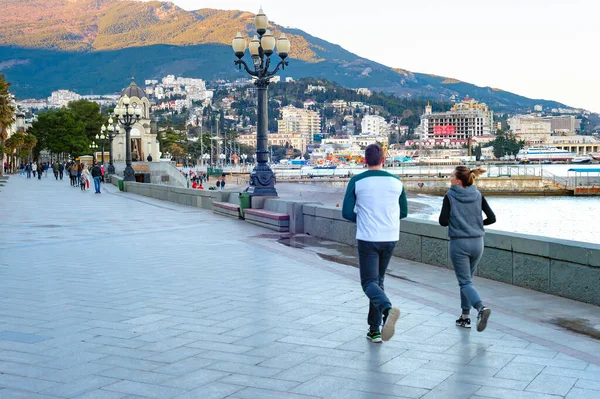 Yalta Crimea エイプリル社2018年3月 海の遊歩道でジョギングをするカップル 歩行者 日没の街並みを背景に山 — ストック写真
