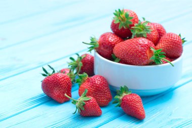 Kırsal beyaz ahşap arka planda seramik kasede taze çilek yığını