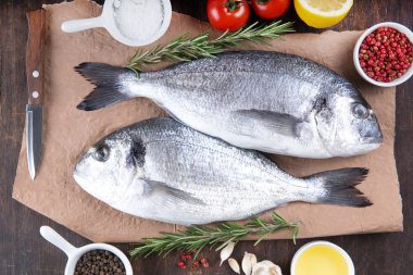 Dorado çiğ balık pişirme ve malzemeler. Dorado, limon, domates, otlar ve baharatlar. Ahşap masa üzerinde Üstten Görünüm