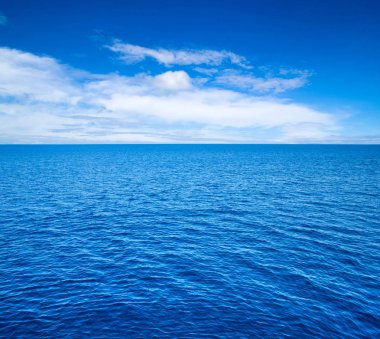 Bulutlar mavi gökyüzünde sakin denizin üzerinde güneş ışığı yansımasıyla