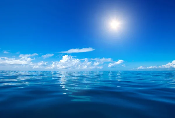 Clouds on blue sky over calm sea with sunlight reflection — Stock Photo, Image