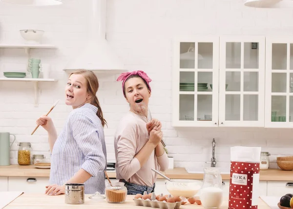 Two cheerful friends cook together desserts and sing.