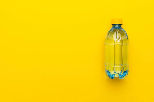 Bottiglia di acqua di plastica con tappo giallo su sfondo giallo con spazio copia — Foto Stock