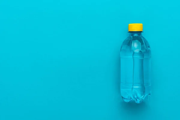 Mavi arka planda sarı kap ile plastik su şişesi — Stok fotoğraf