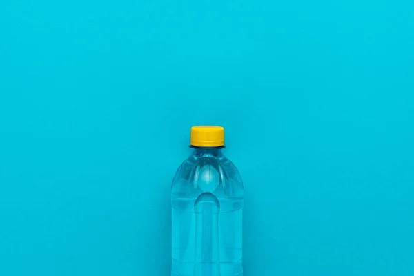 Plastová vodní láhev se žlutým uzávěrem na modrém pozadí — Stock fotografie