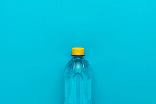 Botella de agua de plástico con tapa amarilla sobre el fondo azul — Foto de Stock