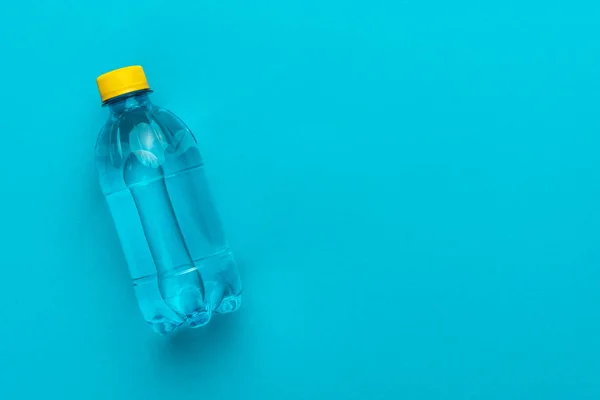 Bottiglia di acqua di plastica con tappo giallo sullo sfondo blu — Foto Stock