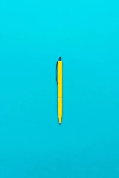minimalist flat lay photo of yellow ballpoint pen over turquoise blue background