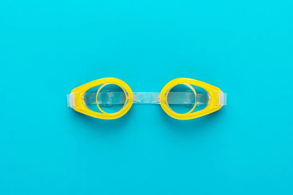 Yellow swimming goggles over blue background with central composition — 스톡 사진