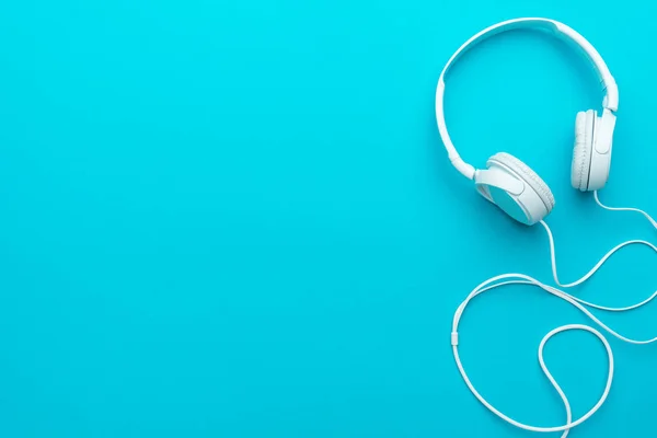 Minimal photo of white headphones with cable on blue background with copy space.