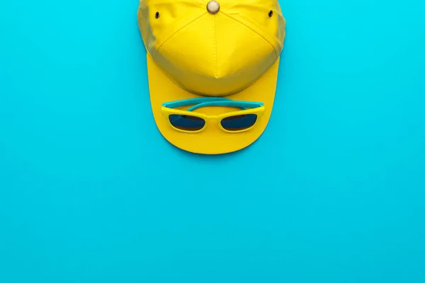 Желтая бейсболка и солнцезащитные очки на синем фоне с копировальным пространством — стоковое фото