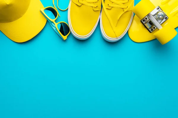 Cappello da baseball giallo, occhiali da sole, scarpe da ginnastica, mini cruiser su sfondo blu — Foto Stock