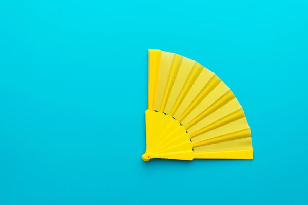 Минималистская фотография жёлтого ручного вентилятора на бирюзовом синем фоне с копировальным пространством — стоковое фото