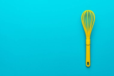 Canlı plastik mutfak gereçleri üst görünüm fotoğraf. Kopya alanı ve sağ yan konumu ile turkuaz mavi arka plan üzerinde sarı çırpıcı minimalist düz yatıyordu görüntü. Mavi masa üzerinde mutfak aleti karıştırma