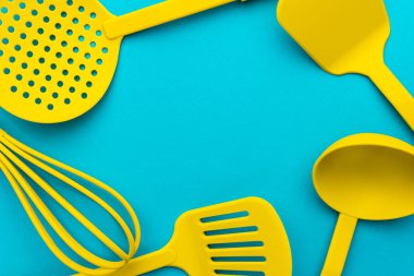 Canlı plastik mutfak gereçleri üst görünüm fotoğraf. Sarı kepçe, çırpma teli, yağsız kaşık ve spatulaların turkuaz mavisi masa arka planı üzerinde, merkezinde kopya alanı olan yakın çekim görüntüsü