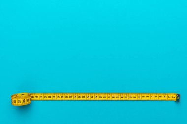 Sarı yumuşak ölçüm bandının üst görünümü. Kopyalama alanı ile turkuaz maviarka plan üzerinde metrik ölçek ile bant ölçüsü Minimalist düz yatıyordu görüntü. Diyet kavramı olarak vücut ölçüm bandı Fotoğrafı