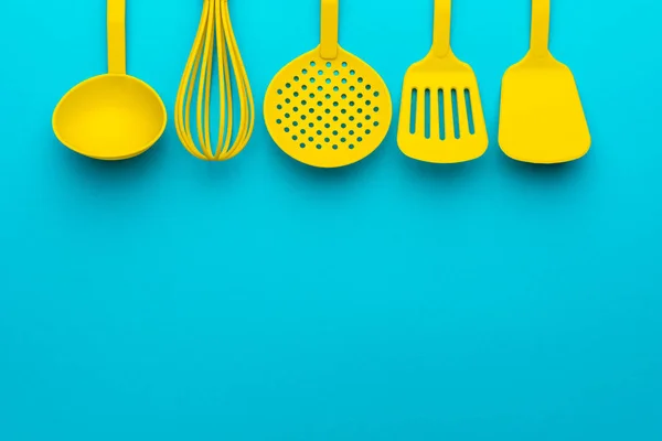 Utensílios de cozinha de plástico amarelo brilhante - conceito de cozinha. Flat lay imagem de concha, batedor, colher de escumadeira e espátulas com espaço de cópia. Posição invertida dos utensílios de cozinha sobre fundo azul-turquesa — Fotografia de Stock