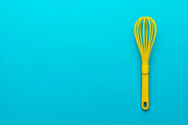 Photo de vue du dessus de l'ustensile de cuisine en plastique vif. Image plate minimaliste du fouet jaune sur fond bleu turquoise avec espace de copie et position du côté droit. Mélange d'outils de cuisine sur table bleue — Photo