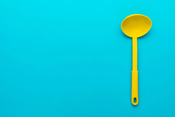 Вид зверху фото яскравого пластикового кухонного посуду. Мінімалістичне плоске зображення жовтого ковша на бірюзовому синьому фоні з копіювальним простором. Права бічна позиція занурювача на синьому столі — стокове фото