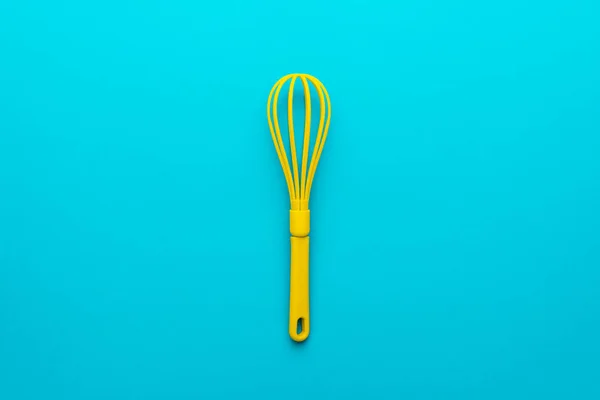 Top view of yellow plastic whisk over turquoise blue background with copy space — Stock Photo, Image