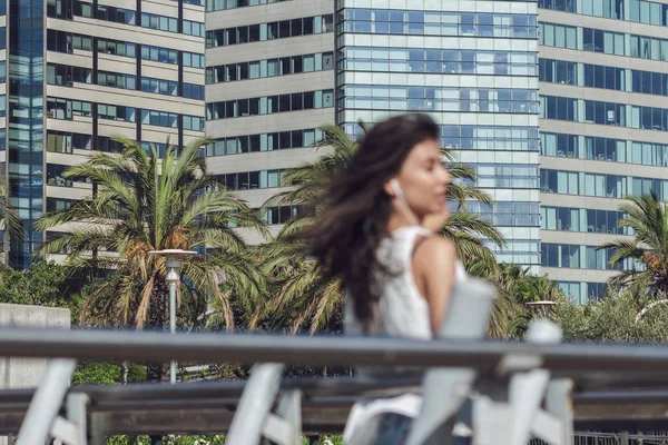 Chica escuchando música fuera de foco en primer plano y fondo de la ciudad moderna —  Fotos de Stock