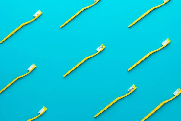 Top view of many new yellow plastic toothbrushes over turquoise blue background — Stock Photo, Image
