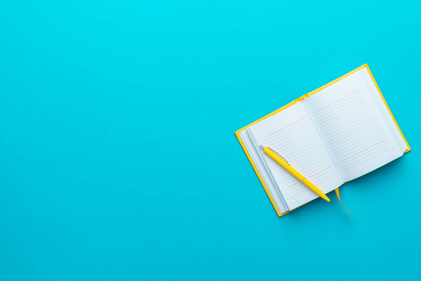 Top view of opened notebook and pen on turquoise blue background with copy space