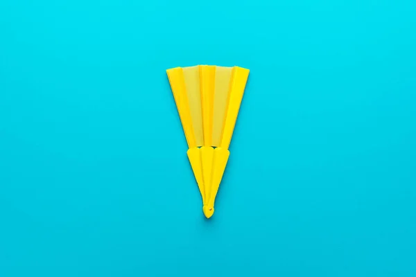 Foto minimalista do ventilador de mão amarelo no fundo azul-turquesa com espaço de cópia — Fotografia de Stock