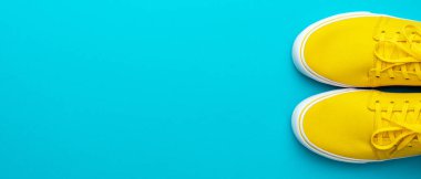 Kopya alanı olan kaykay ayakkabılarının en üst görüntüsü. Turkuaz mavi arka planda bir çift sarı spor ayakkabı. Bağcıklı sarı spor ayakkabıların minimalist fotoğrafı. Sarı yaz ayakkabılarının düz görüntüsü