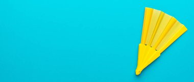 Sarı el vantilatörünün üst görüntüsü. Fotokopi alanı olan turkuaz mavi arka plan. Sağ yan kompozisyonu olan canlı plastik katlama vantilatörünün minimalist düz yatay fotoğrafı.