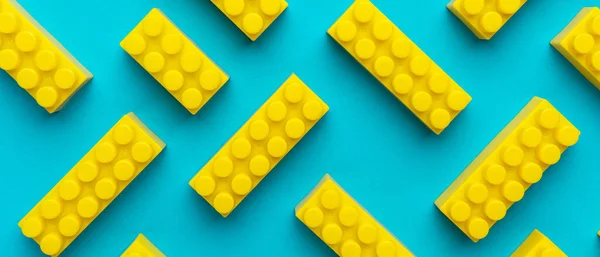 Top view of plastic blocks background. Flat lay image of toy background made with yellow building blocks from child constructor. Bright yellow plastic building blocks on turquoise blue background.