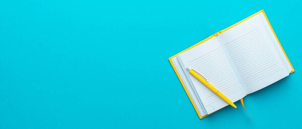Top view of opened notebook and pen on turquoise blue background with copy space