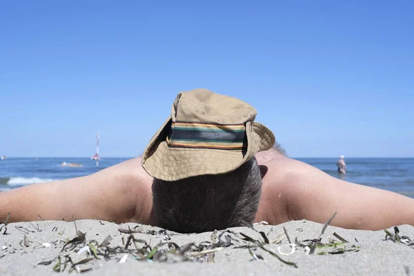 man sunbathes on the beach with a cap on the head