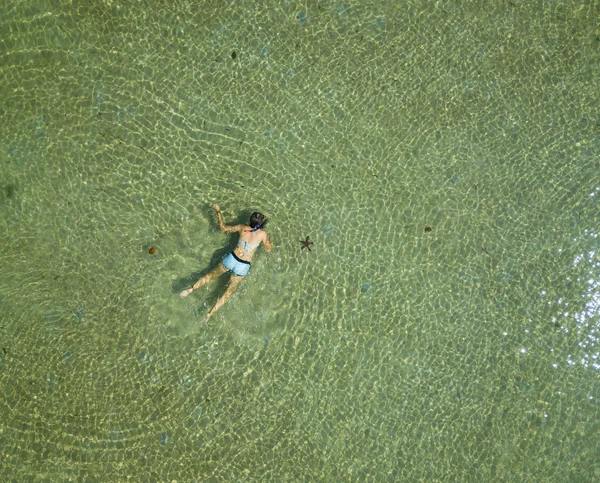 Luftaufnahme einer schwimmenden Frau im Wasser. Sommerlandschaft mit Mädchen, klares azurblaues Wasser, Wellen bei Sonnenaufgang. transparentes Wasser. Draufsicht von der fliegenden Drohne. — Stockfoto