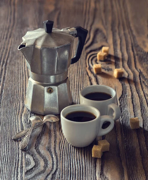 Duas xícaras de café com pedaços de açúcar de cana e cafeteira italiana em uma mesa de madeira. Imagem tonificada . Fotografia De Stock