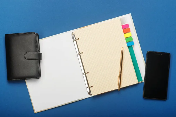 Notebook, penna e smartphone su sfondo blu — Foto Stock