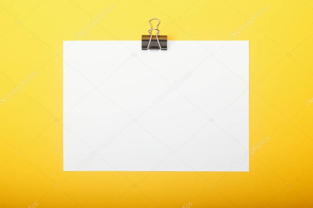 Blank paper with clamp on yellow background. Education concept with copy space for your ideas.