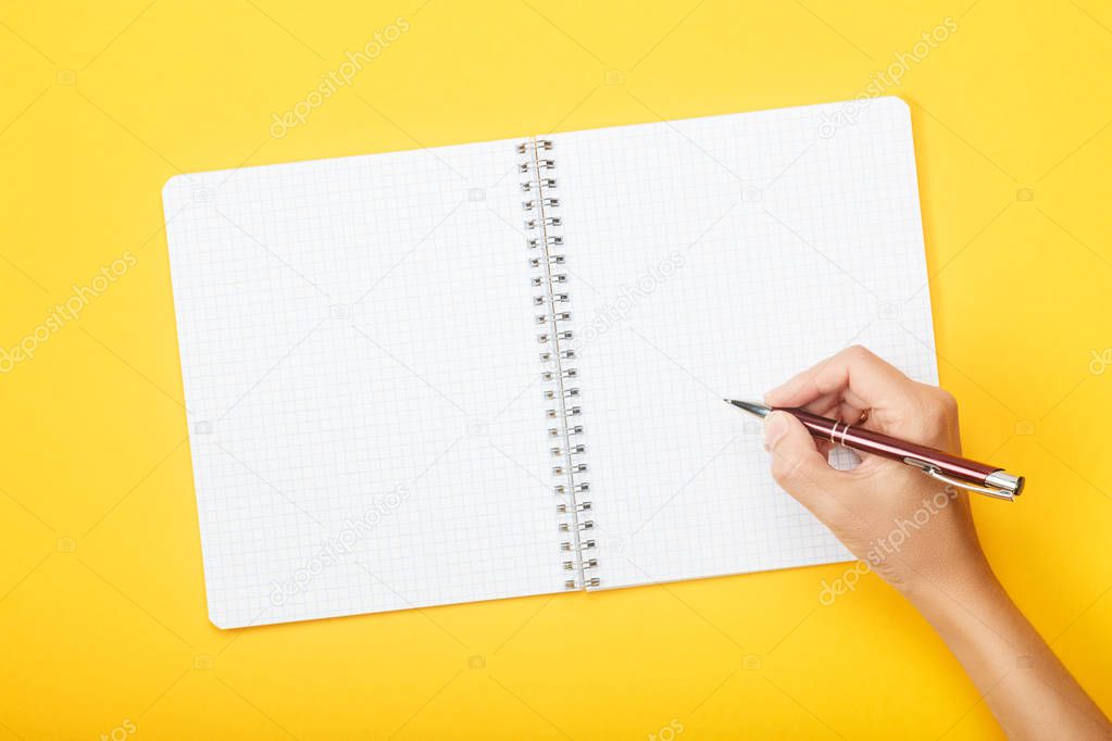 Hand with pen over blank notebook on a yellow background. Mock up with copy space for your ideas.