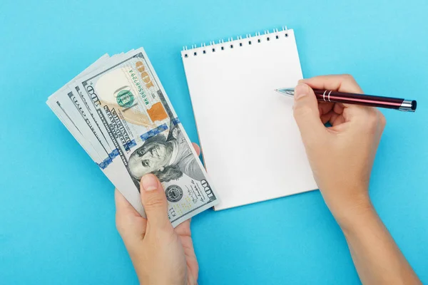 A woman holds money in her hand and writing in a notebook on a blue background — Stock Photo, Image