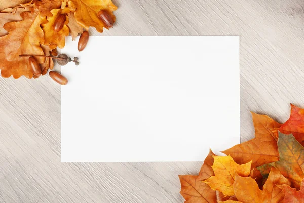 Papel blanco en blanco sobre fondo de textura de madera con hojas de arce y roble, bellotas — Foto de Stock