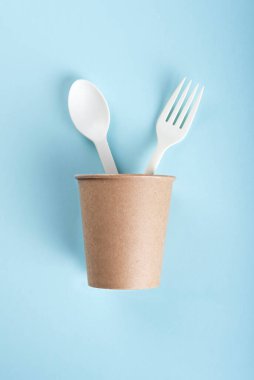 Açık mavi arka planda çatallı ve kaşıklı biyolojik çözünebilir bardak..