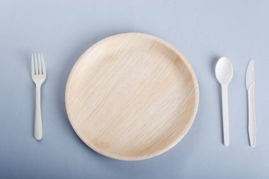 Açık gri arka planda tek kullanımlık tabak, çatal, kaşık ve bıçak.